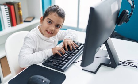 Téléchargez les photos : Adorable étudiante hispanique utilisant l'ordinateur assis sur la table en classe - en image libre de droit