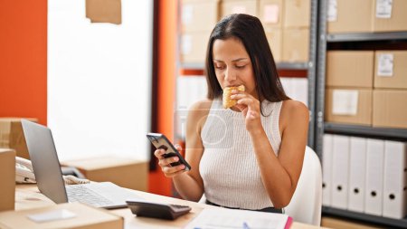 Photo for Young beautiful hispanic woman ecommerce business worker eating croissant working at office - Royalty Free Image
