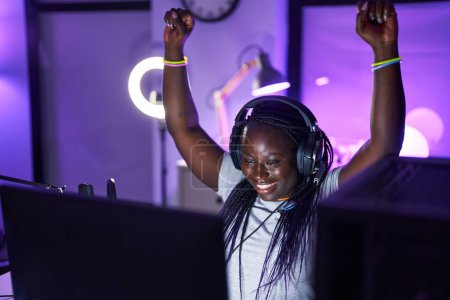 Téléchargez les photos : African american woman streamer jouer à un jeu vidéo avec l'expression gagnante à la salle de jeux - en image libre de droit