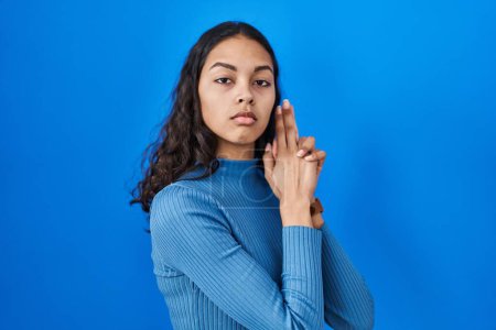 Photo for Young brazilian woman standing over blue isolated background holding symbolic gun with hand gesture, playing killing shooting weapons, angry face - Royalty Free Image