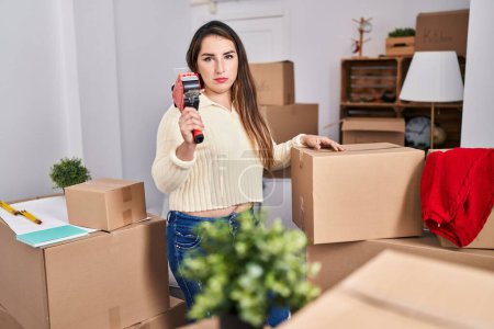 Photo for Young hispanic woman moving to a new home packing boxes thinking attitude and sober expression looking self confident - Royalty Free Image