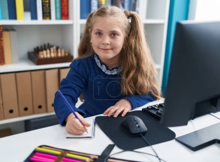 Foto de Adorable estudiante rubia usando notas de escritura por computadora en el aula - Imagen libre de derechos