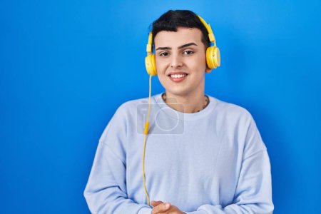 Photo for Non binary person listening to music using headphones with hands together and crossed fingers smiling relaxed and cheerful. success and optimistic - Royalty Free Image
