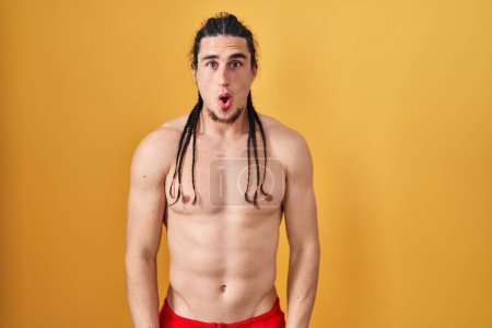 Photo for Hispanic man with long hair standing shirtless over yellow background afraid and shocked with surprise and amazed expression, fear and excited face. - Royalty Free Image