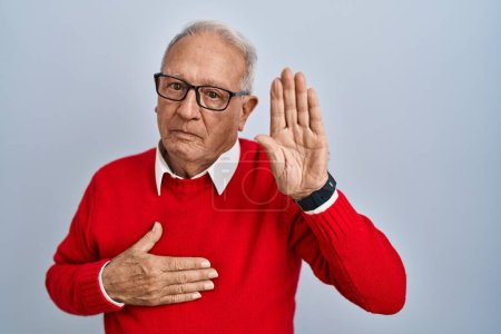 Foto de Hombre mayor con el pelo gris de pie sobre fondo aislado jurando con la mano en el pecho y la palma abierta, haciendo una promesa de lealtad juramento - Imagen libre de derechos