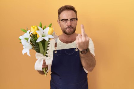 Téléchargez les photos : Middle age man with beard florist shop holding flowers showing middle finger, impolite and rude fuck off expression - en image libre de droit