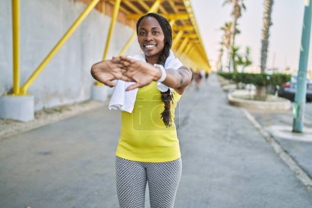 Téléchargez les photos : Femme afro-américaine portant des vêtements de sport étirant le bras dans la rue - en image libre de droit