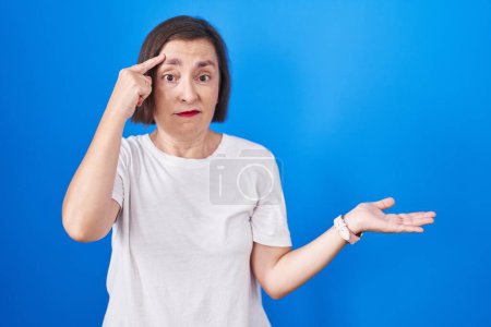 Téléchargez les photos : Middle age hispanic woman standing over blue background confused and annoyed with open palm showing copy space and pointing finger to forehead. think about it. - en image libre de droit