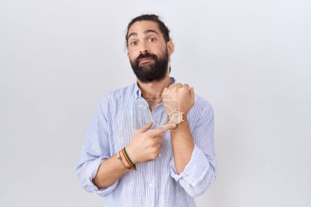 Téléchargez les photos : Homme hispanique à la barbe portant une chemise décontractée à la hâte pointant vers le temps de montre, impatience, regardant la caméra avec une expression détendue - en image libre de droit