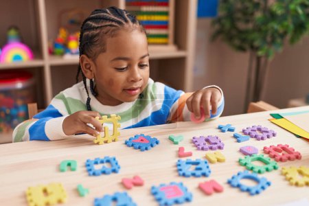 Téléchargez les photos : Garçon afro-américain jouer avec le jeu de puzzle de vocabulaire assis sur la table à la maternelle - en image libre de droit