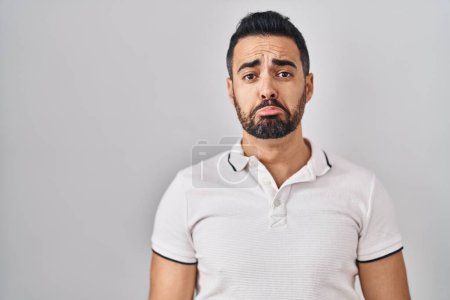 Foto de Joven hombre hispano con barba vistiendo ropa casual sobre fondo blanco deprimido y preocupado por la angustia, llorando enojado y asustado. expresión triste. - Imagen libre de derechos