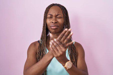 Foto de Mujer afroamericana de pie sobre fondo rosa sufriendo dolor en manos y dedos, inflamación de la artritis - Imagen libre de derechos