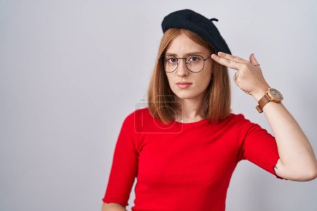 Photo for Young redhead woman standing wearing glasses and beret shooting and killing oneself pointing hand and fingers to head like gun, suicide gesture. - Royalty Free Image