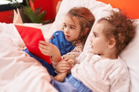 Téléchargez les photos : Adorable livre de lecture de filles couché sur le lit dans la chambre - en image libre de droit