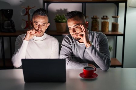Photo for Homosexual couple using computer laptop mouth and lips shut as zip with fingers. secret and silent, taboo talking - Royalty Free Image