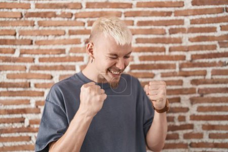 Photo for Young caucasian man standing over bricks wall very happy and excited doing winner gesture with arms raised, smiling and screaming for success. celebration concept. - Royalty Free Image