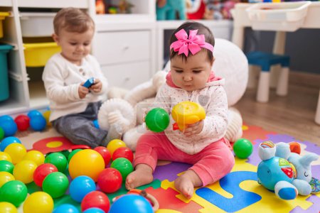 Foto de Adorable niño y niña jugando con bolas sentados en el suelo en el jardín de infantes - Imagen libre de derechos