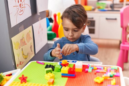 Foto de Adorable niño hispano jugando con bloques de construcción sentado en la mesa en el jardín de infantes - Imagen libre de derechos