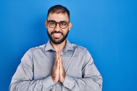 Photo for Middle east man with beard standing over blue background praying with hands together asking for forgiveness smiling confident. - Royalty Free Image