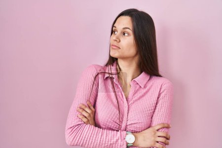 Téléchargez les photos : Young hispanic woman standing over pink background looking to the side with arms crossed convinced and confident - en image libre de droit