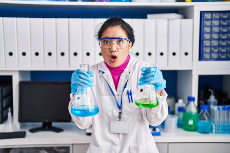 Téléchargez les photos : Jeune femme asiatique travaillant au laboratoire scientifique effrayé et choqué par l'expression surprise et étonnée, la peur et le visage excité. - en image libre de droit