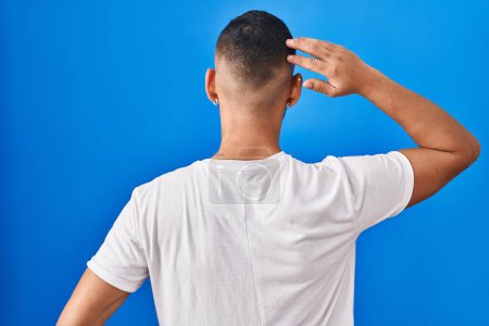 Téléchargez les photos : Jeune homme hispanique debout sur fond bleu vers l'arrière pensant au doute avec la main sur la tête - en image libre de droit