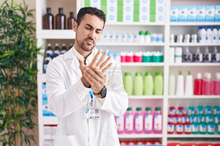 Photo for Handsome hispanic man working at pharmacy drugstore suffering pain on hands and fingers, arthritis inflammation - Royalty Free Image