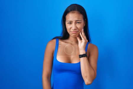 Photo for Hispanic woman standing over blue background touching mouth with hand with painful expression because of toothache or dental illness on teeth. dentist - Royalty Free Image