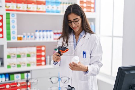 Téléchargez les photos : Jeune fille hispanique pharmacien numérisation pilules bouteille à la pharmacie - en image libre de droit
