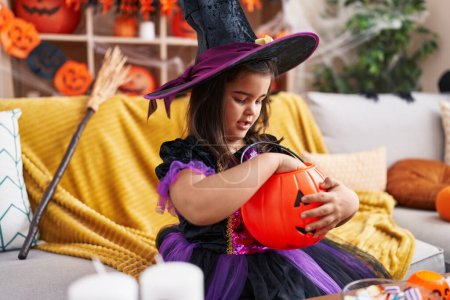 Foto de Adorable chica hispana teniendo fiesta de halloween sosteniendo dulce de canasta de calabaza en casa - Imagen libre de derechos