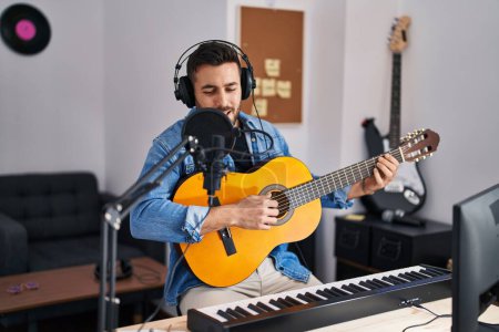 Photo for Young hispanic man singing song playing classical guitar at music studio - Royalty Free Image
