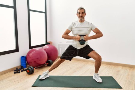 Photo for Middle age grey-haired man smiling confident using kettlebell training at sport center - Royalty Free Image