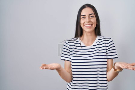 Téléchargez les photos : Jeune femme brune portant t-shirt rayé souriant gai offrant des mains donnant assistance et acceptation. - en image libre de droit