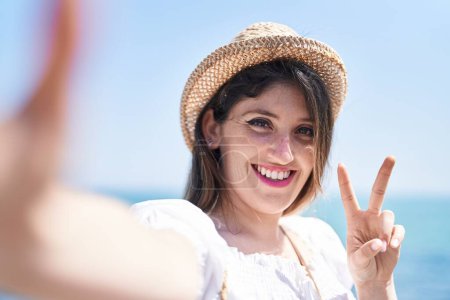 Foto de Young hispanic woman tourist smiling confident make selfie by camera at seaside - Imagen libre de derechos