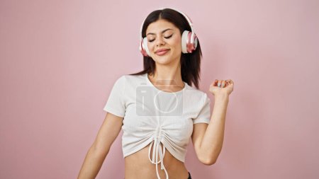 Young caucasian woman listening to music and dancing over isolated pink background