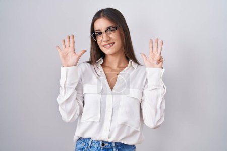 Foto de Mujer morena joven con gafas mostrando y señalando hacia arriba con los dedos número nueve mientras sonríe confiado y feliz. - Imagen libre de derechos