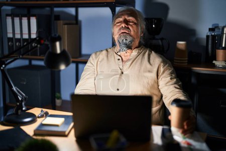 Photo for Middle age man with grey hair working at the office at night looking sleepy and tired, exhausted for fatigue and hangover, lazy eyes in the morning. - Royalty Free Image