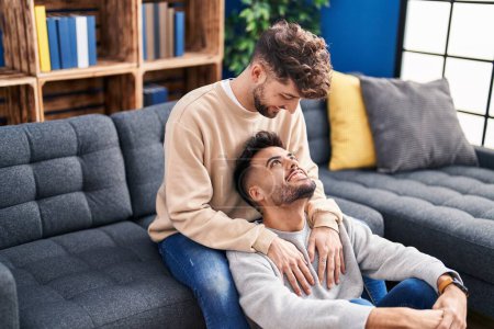 Téléchargez les photos : Jeune couple s'embrassant assis sur le canapé à la maison - en image libre de droit