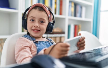 Photo for Adorable hispanic girl student using smartphone and headphones at classroom - Royalty Free Image