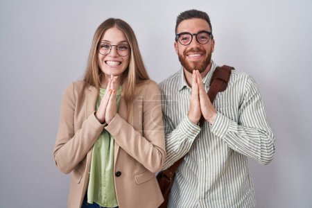 Téléchargez les photos : Jeune couple debout sur fond blanc priant avec les mains ensemble demandant pardon en souriant confiant. - en image libre de droit