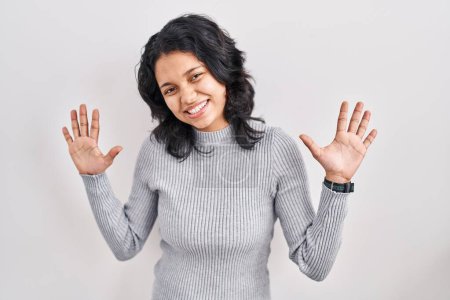 Foto de Mujer hispana con el pelo oscuro de pie sobre el fondo aislado mostrando y señalando hacia arriba con los dedos número diez mientras sonríe confiado y feliz. - Imagen libre de derechos