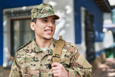 Téléchargez les photos : Jeune homme soldat de l'armée souriant confiant debout dans la rue - en image libre de droit