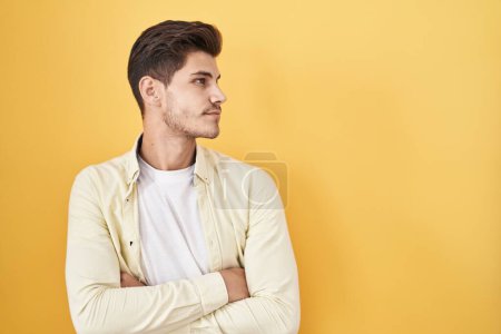 Téléchargez les photos : Jeune homme hispanique debout sur fond jaune regardant du côté avec les bras croisés convaincu et confiant - en image libre de droit