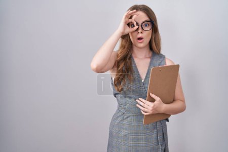 Téléchargez les photos : Femme caucasienne portant des lunettes et des vêtements de travail faisant un geste correct choqué par le visage surpris, les yeux regardant à travers les doigts. expression incrédule. - en image libre de droit