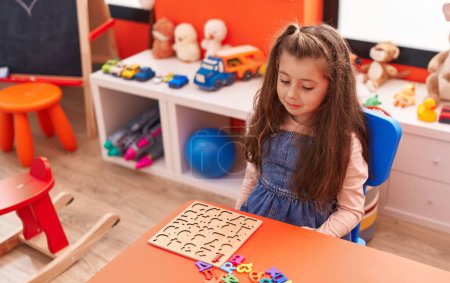 Foto de Adorable chica hispana jugando con matemáticas juego de puzzle sentado en la mesa en el jardín de infantes - Imagen libre de derechos