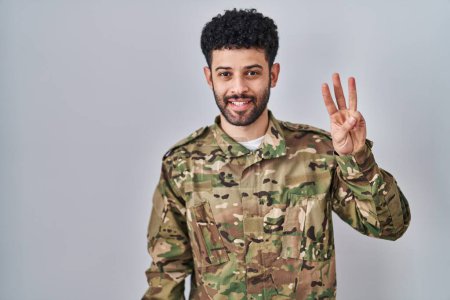 Foto de Hombre árabe con camuflaje uniforme del ejército mostrando y señalando hacia arriba con los dedos número tres mientras sonríe confiado y feliz. - Imagen libre de derechos