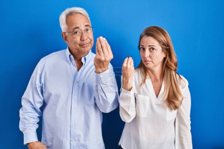 Photo for Middle age hispanic couple standing over blue background doing italian gesture with hand and fingers confident expression - Royalty Free Image