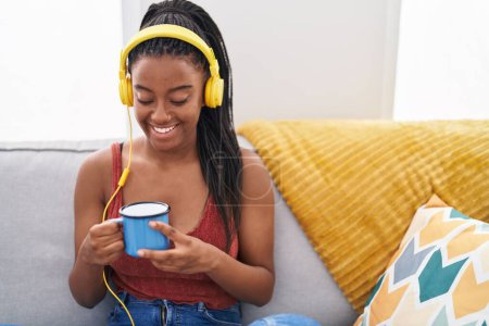 Photo for African american woman listening to music drinking coffee at home - Royalty Free Image