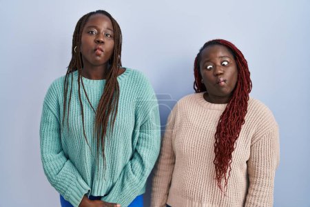 Photo for Two african woman standing over blue background making fish face with lips, crazy and comical gesture. funny expression. - Royalty Free Image