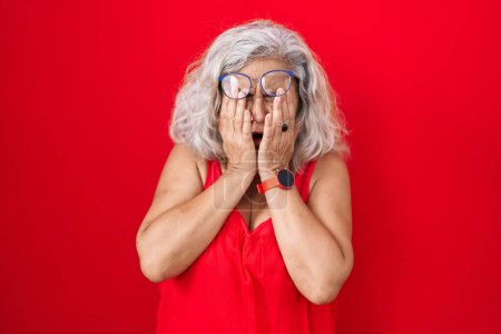 Téléchargez les photos : Femme d'âge moyen avec les cheveux gris debout sur fond rouge frottant les yeux pour la fatigue et les maux de tête, somnolent et l'expression fatiguée. problème de vision - en image libre de droit